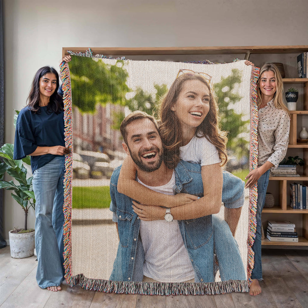 Two people holding up the woven photo blanket indoors to show its size